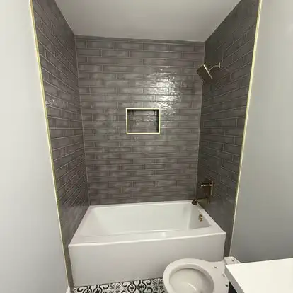 A bathroom with a gray tiled shower surround and a new tub