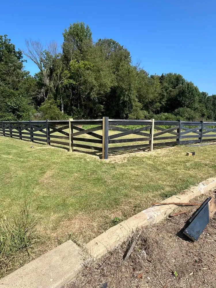 A black ranch style fence along a field